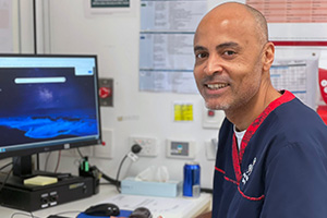 A male Peel Health Campus emergency department nurse sits at a computer