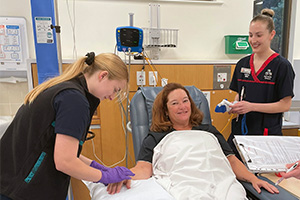Two Peel Health Campus renal nurses stand either side of a female patient in a treatment chair