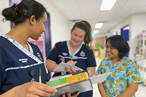 Three Peel Health Campus nurses stand together reviewing documents